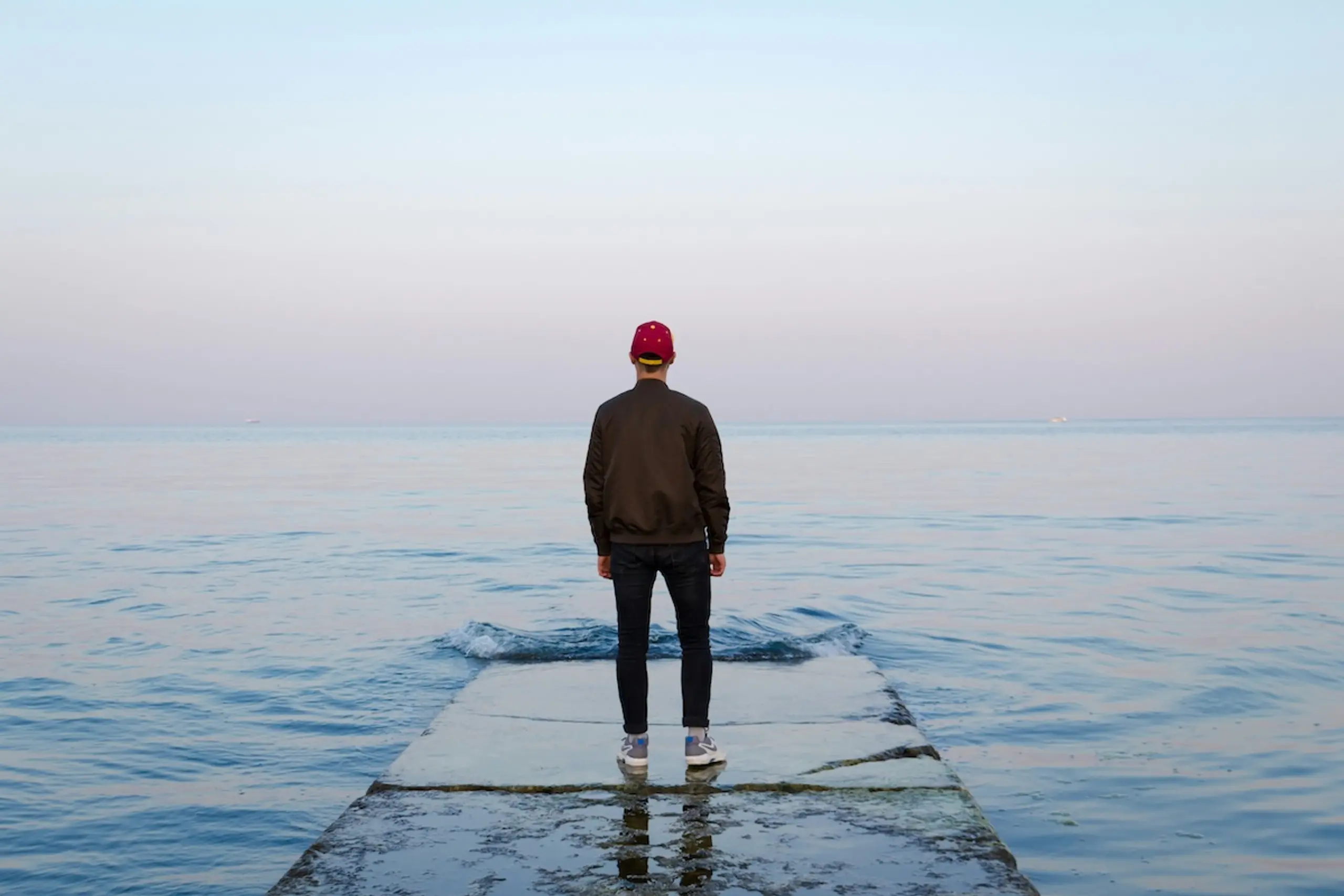 man wearing hat on pier looking out onto water and horizon