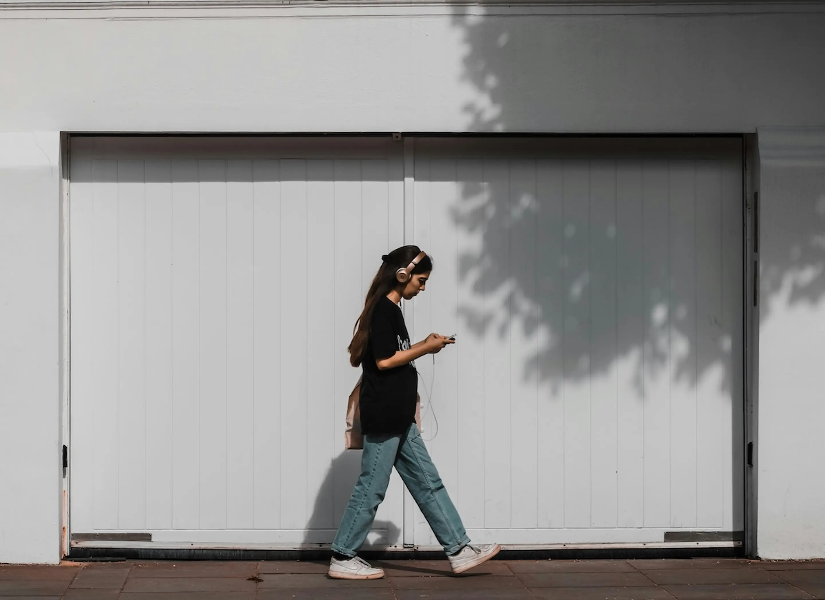 woman walking on sidewalk in front of garage with headphones