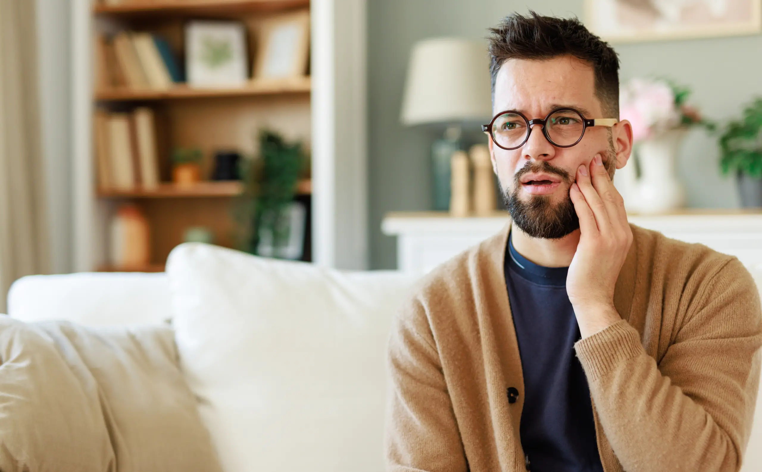 Man in glasses on couch touches jaw