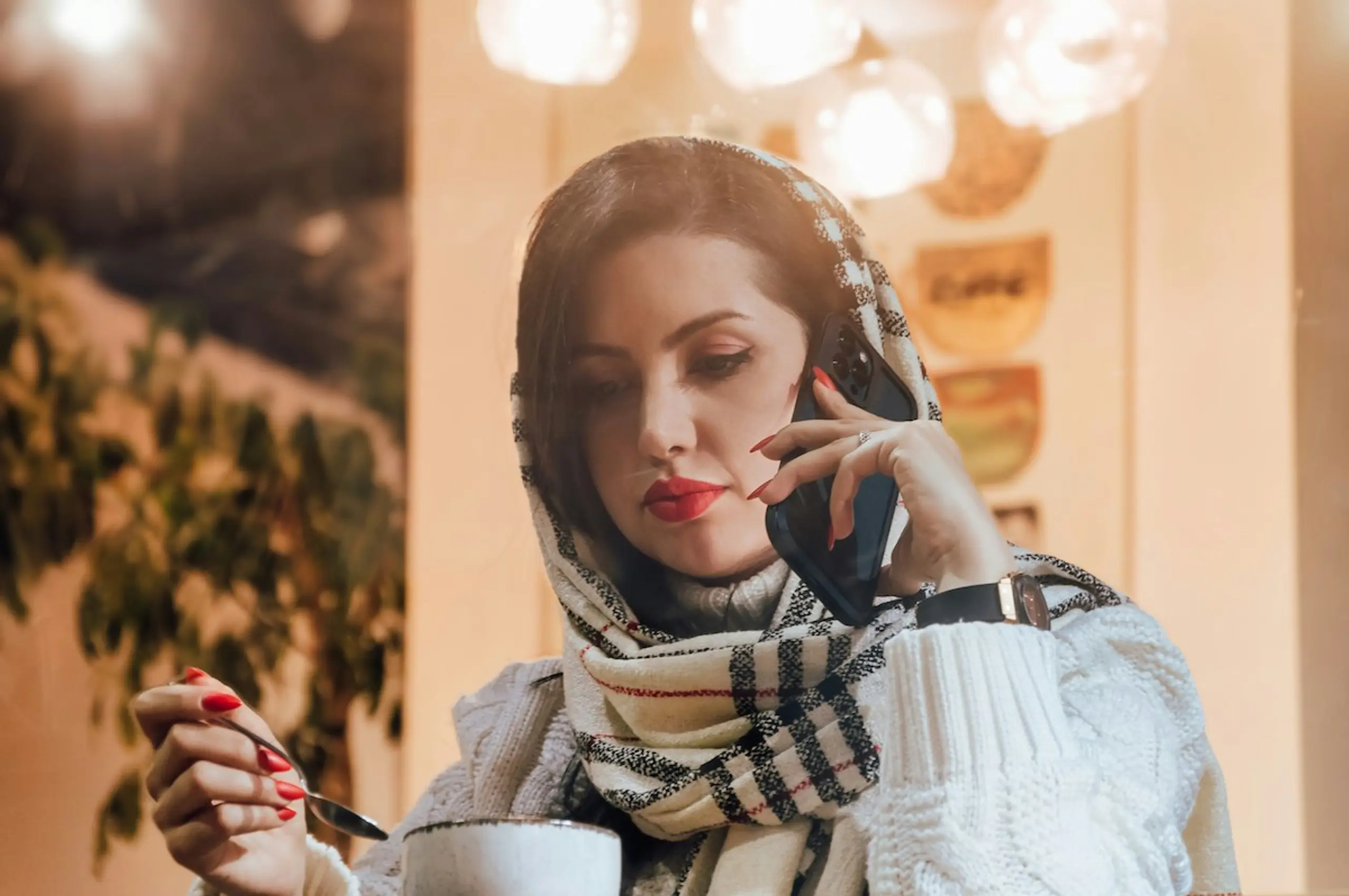 A woman on the phone while at a cafe drinking tea