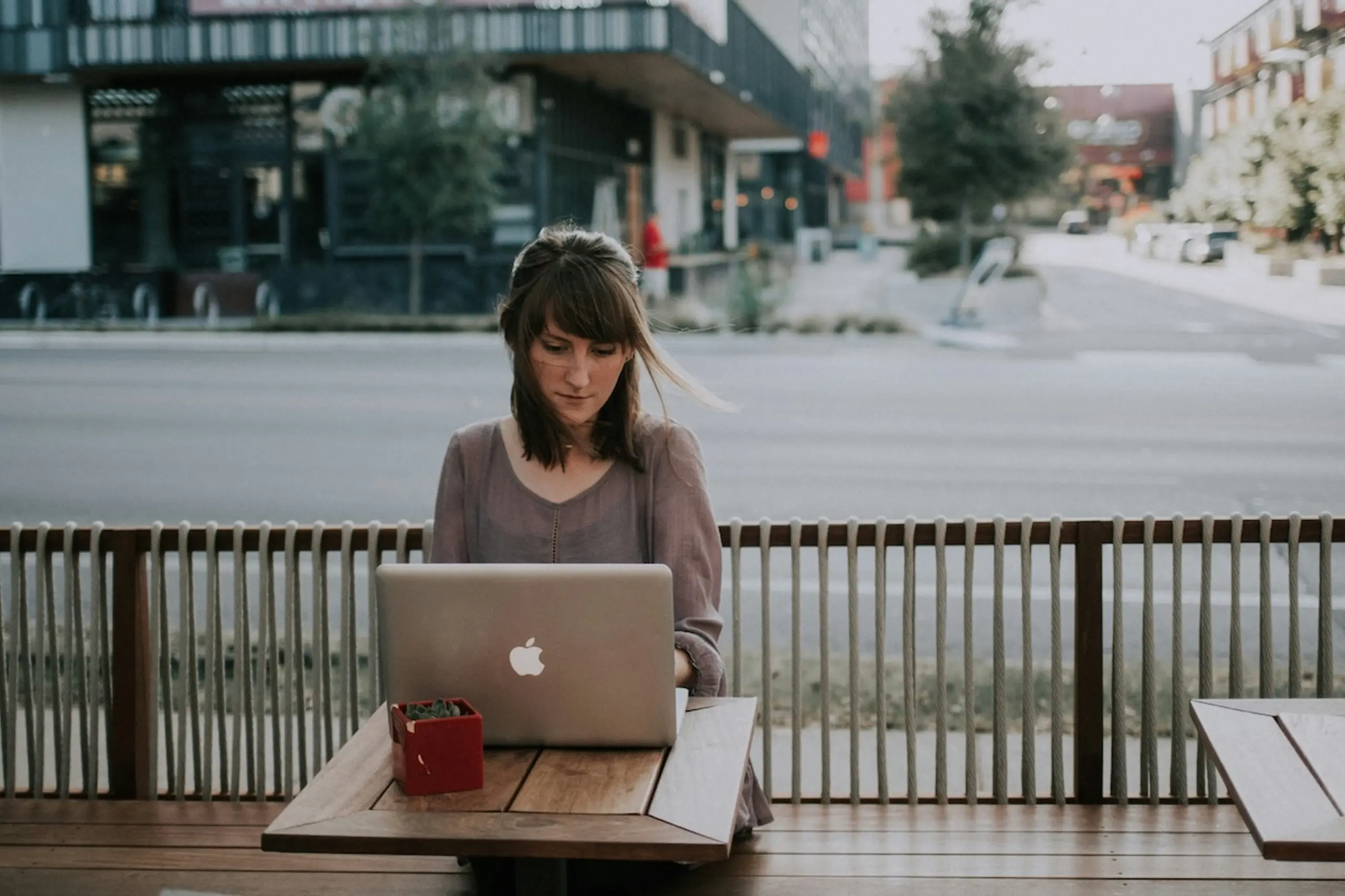 woman sitting at table in city next to the street with a macbook
