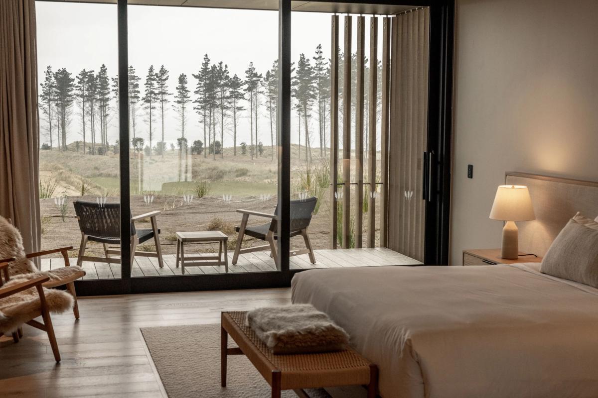 The Ocean Restaurant at Te Arai Links overlooking the 18th green of the South Course at dusk with diners at table and the Northland coastline visible through the floor to ceiling windows with the Pacific Ocean beyond