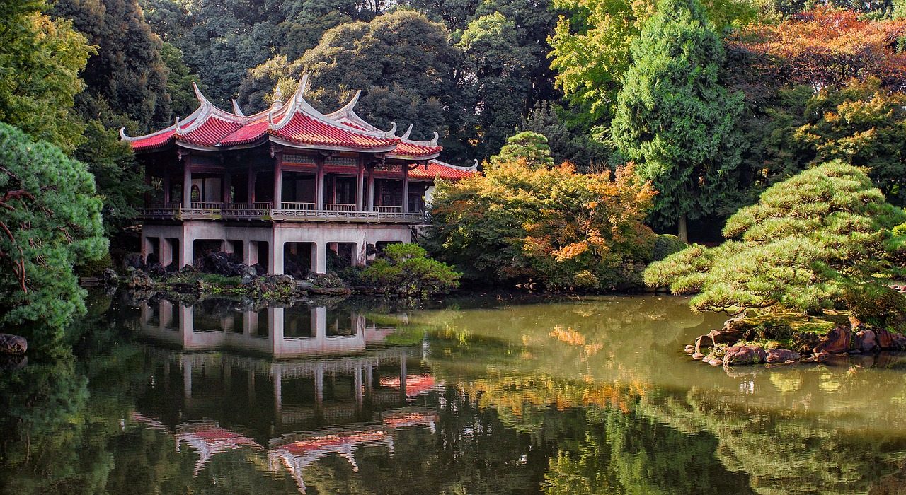 A red-roofed pavilion reflected in a pond surrounded by colorful trees.