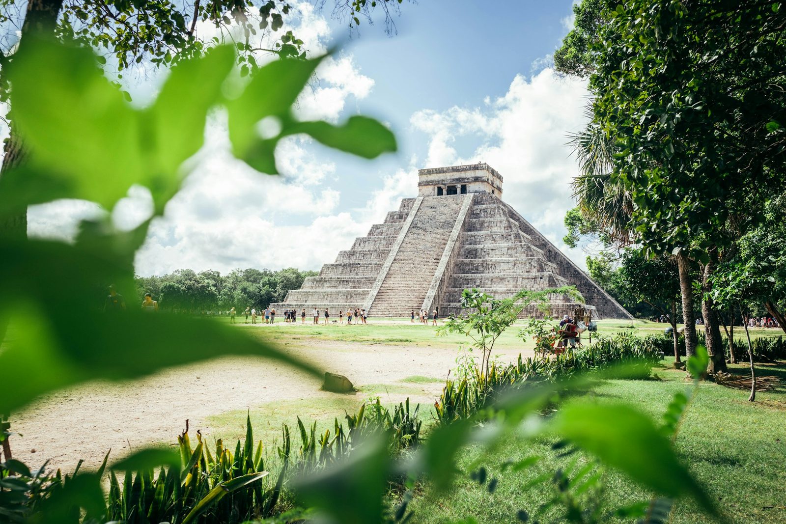 A stone pyramid framed by green trees and leaves beneath a blue sky in Mexico.