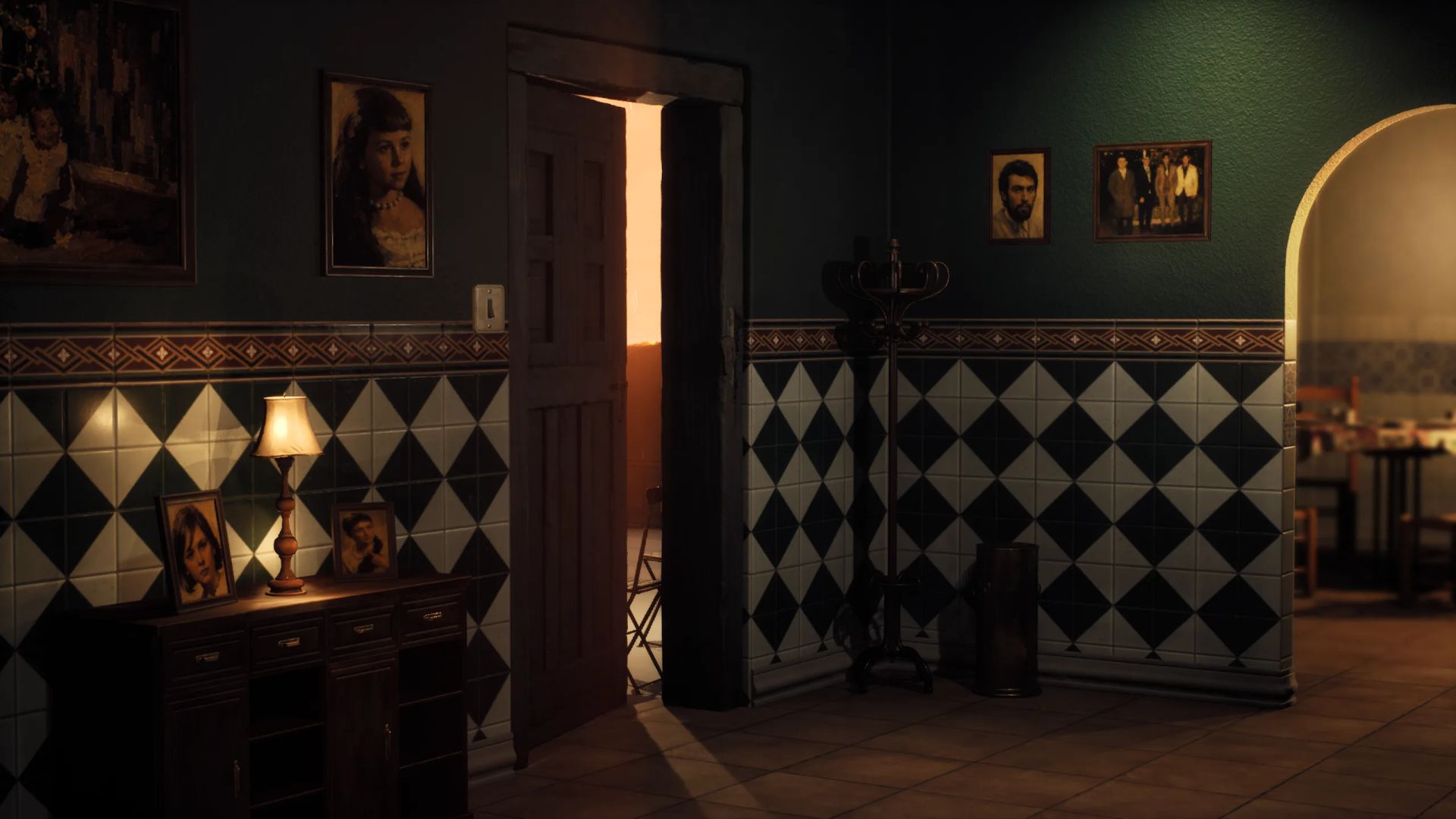Dim entrance hall with green and black diamond tiles, family portraits, a table lamp and an open door