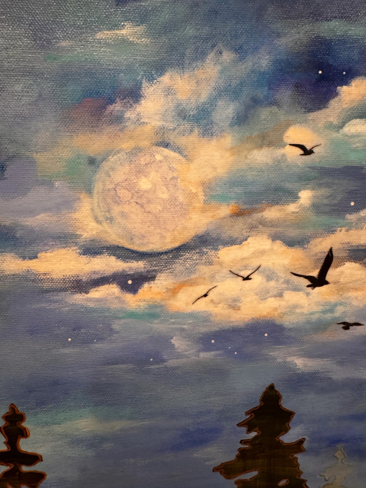 Full moon glowing through blue and cream clouds as dark birds cross above silhouetted evergreens.