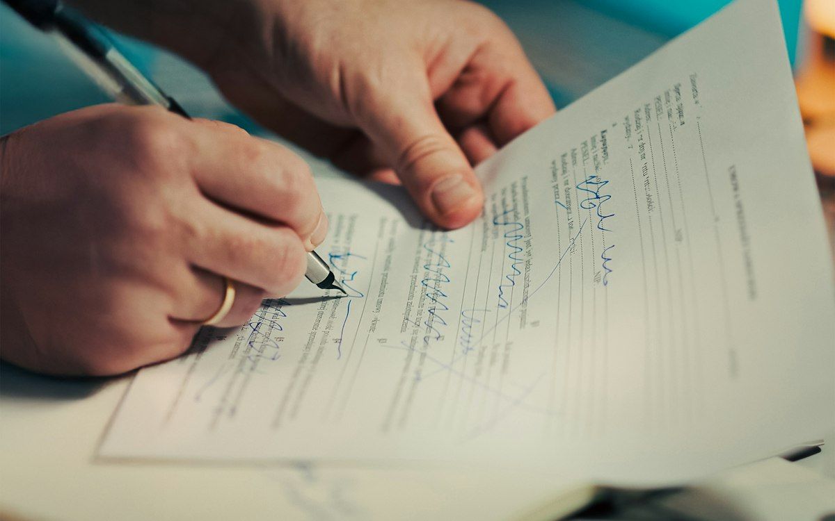 A person signing a document with a pen at a desk