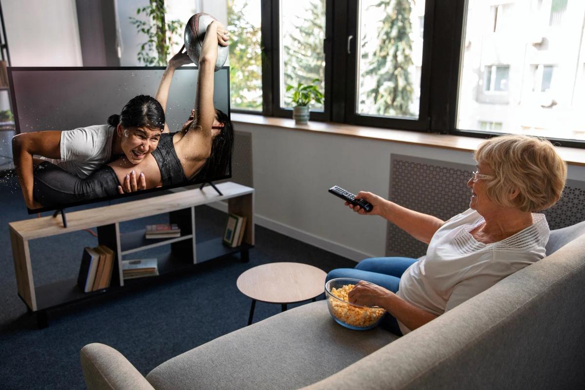 Femme regardant un match de sport en 4K HDR sur IPTV depuis son canapé, télécommande en main et bol de popcorn, dans un salon lumineux