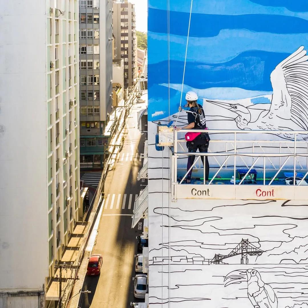 Tuane Arte pintando mural em prédio com andaime suspenso em Florianópolis