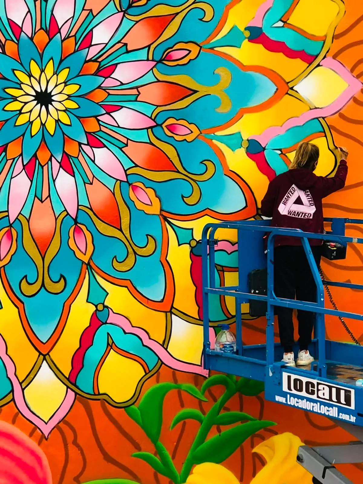 Tuane Arte pintando mural de mandala em plataforma elevatória