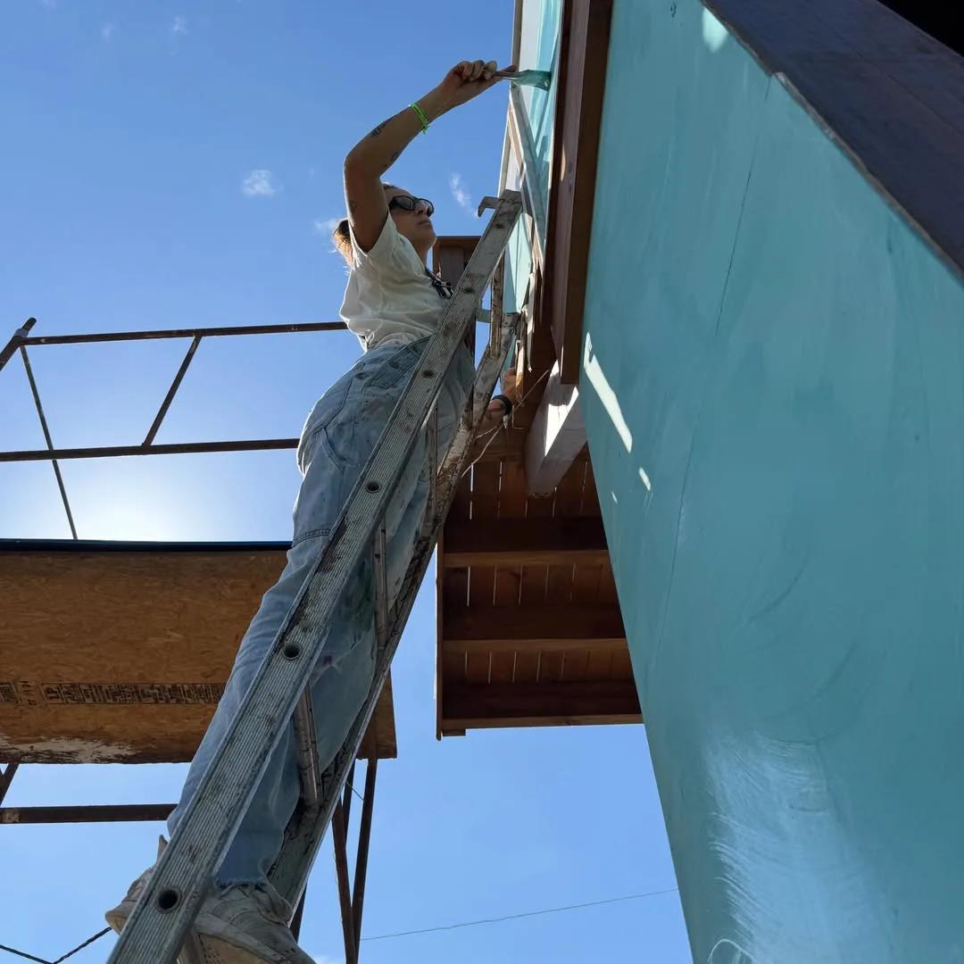 Tuane Arte pintando estrutura à beira-mar em uma escada