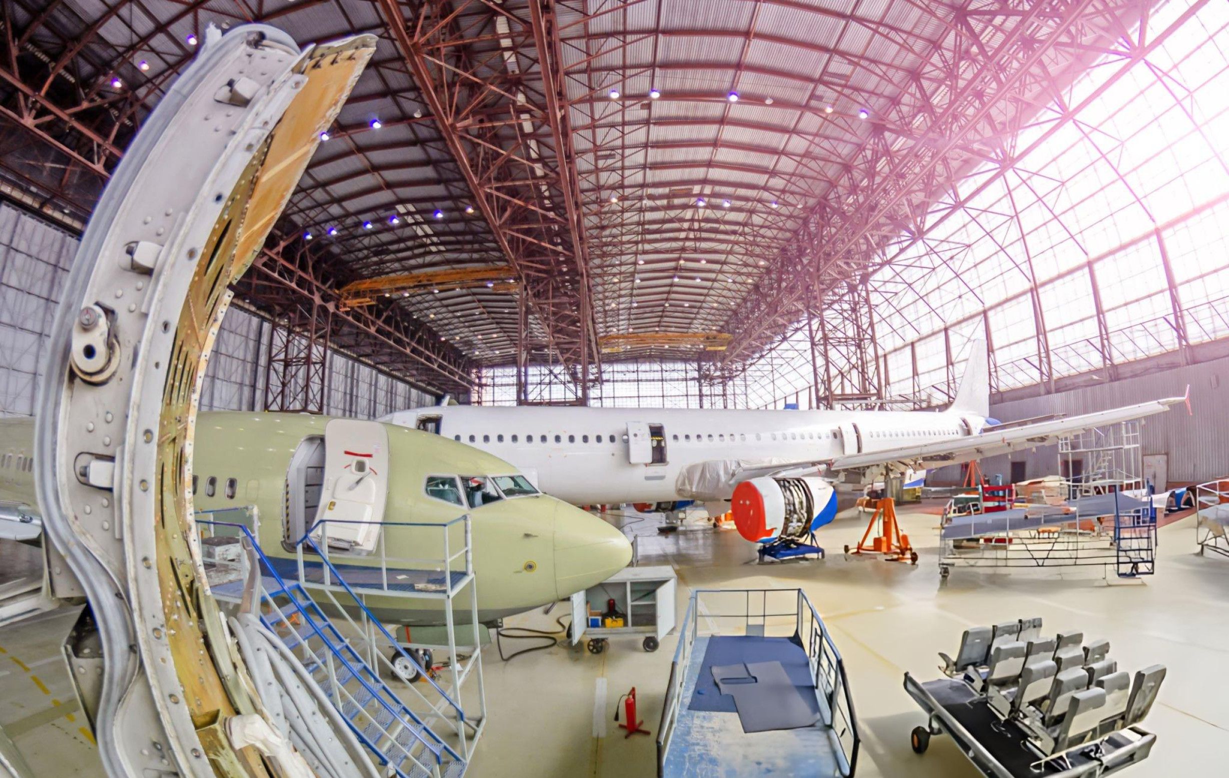  An aircraft manufacturing plant showcasing the assembly process of different types of aircraft by a dedicated workforce.