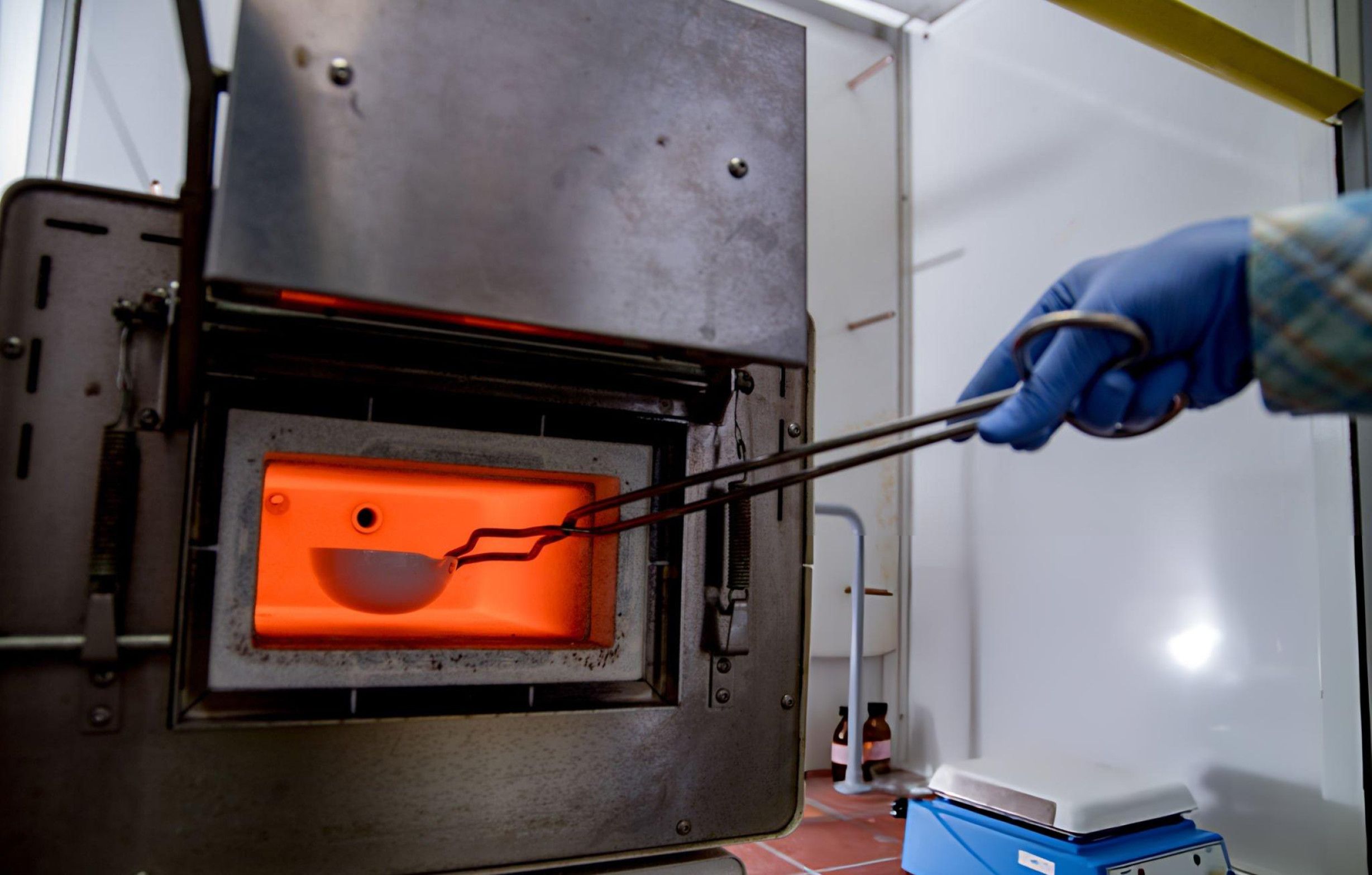 A laboratory technician examines a sample within a furnace, focusing on accurate testing and experimental results.