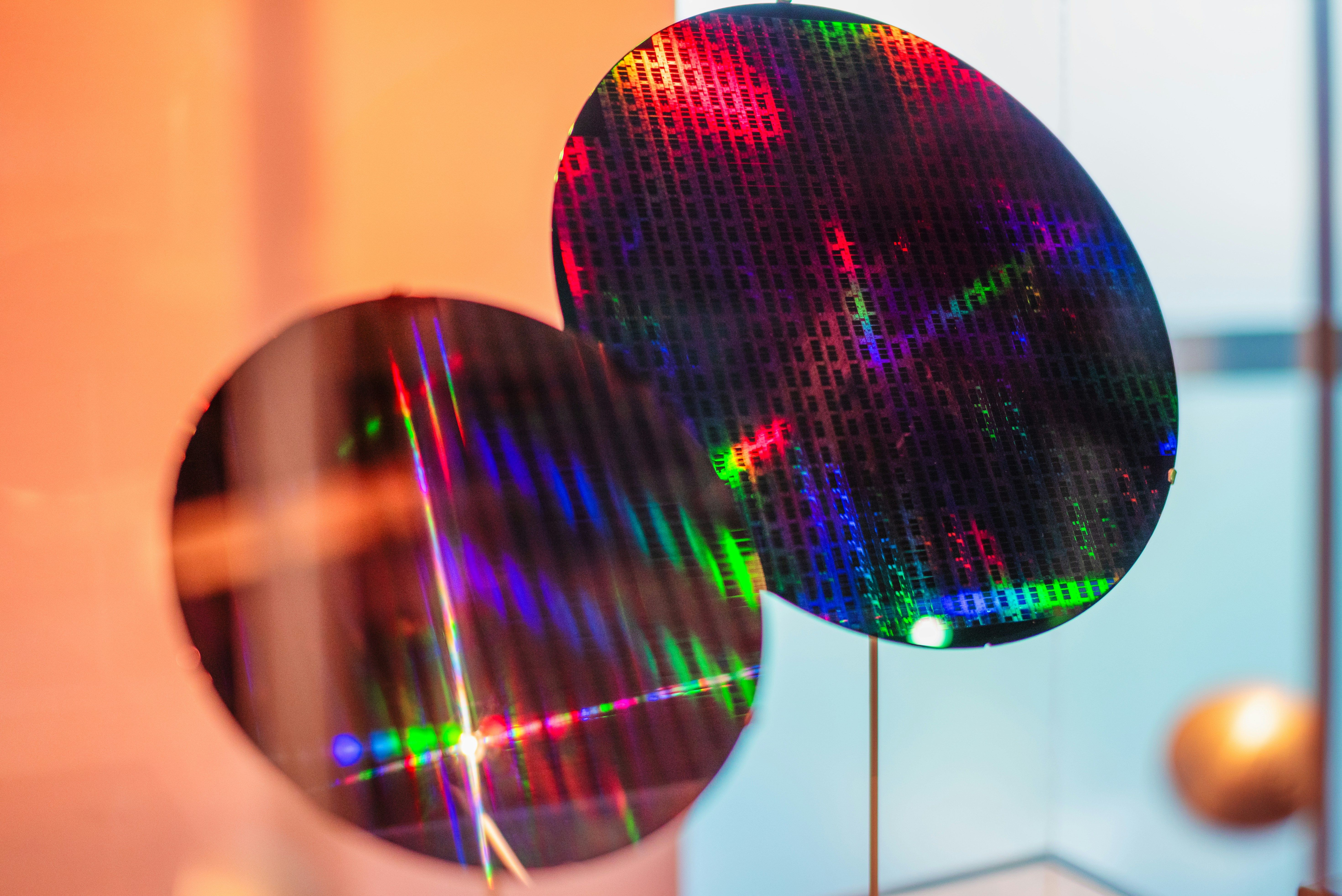 A silicon wafer displayed on a flat surface, featuring a shiny, reflective surface with detailed micro-patterns.
