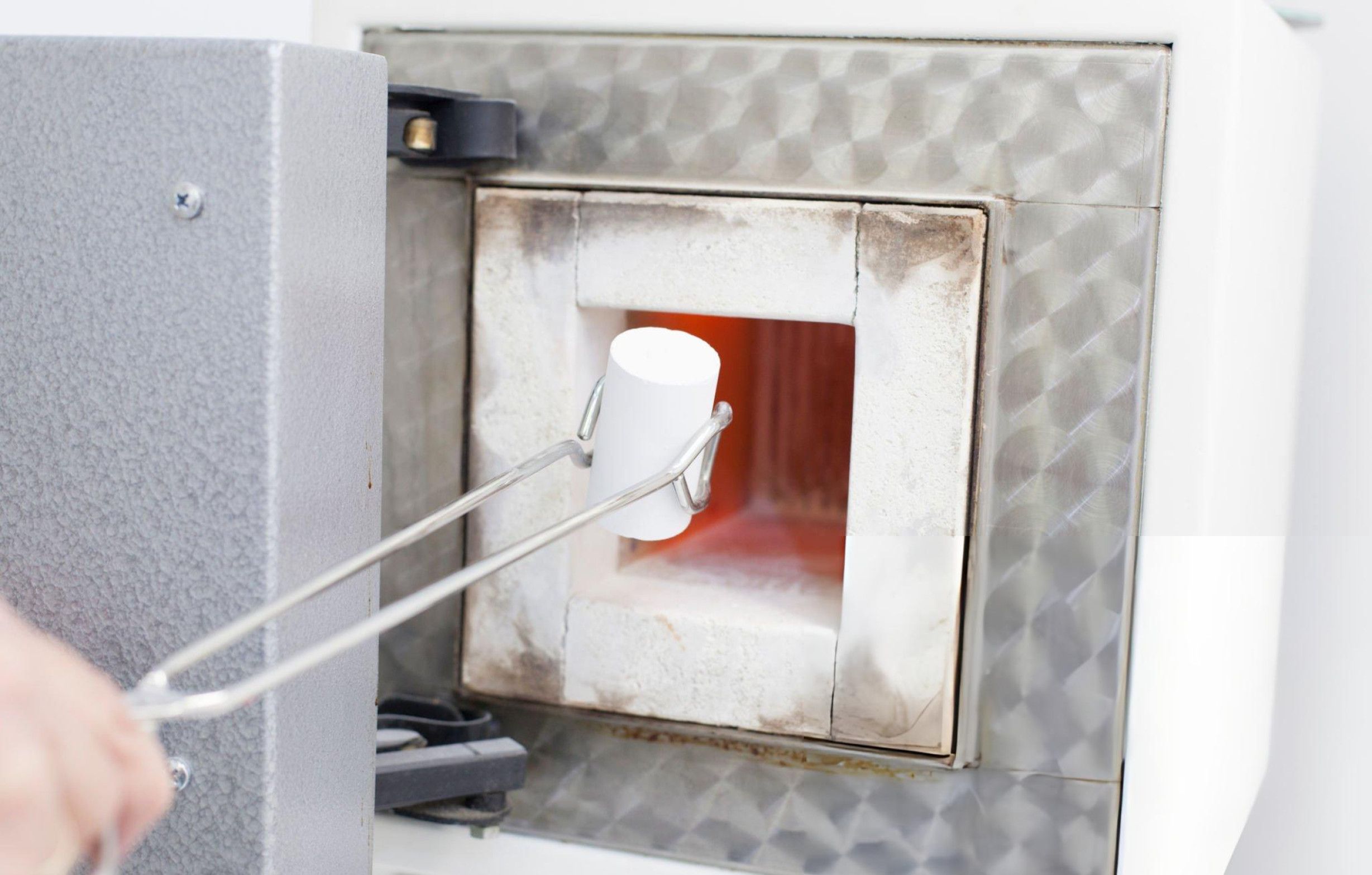 A dental technician operates a burnout furnace to remove wax patterns, ensuring precision in dental prosthetic fabrication.