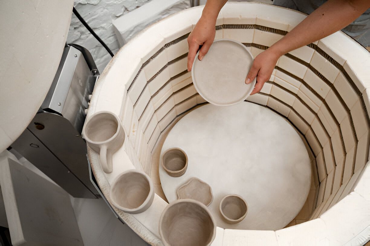 A person carefully places ceramic items into a muffle furnace for the firing process.