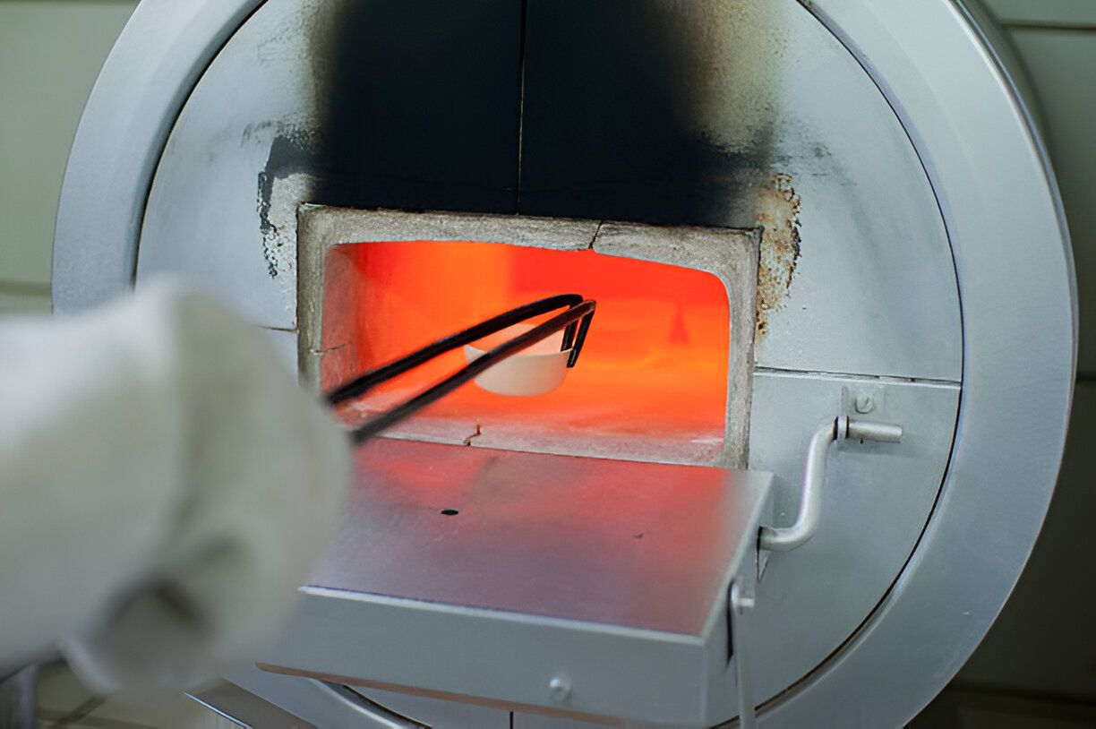 A technician is positioning a sample inside a laboratory furnace, preparing for a controlled heating process.