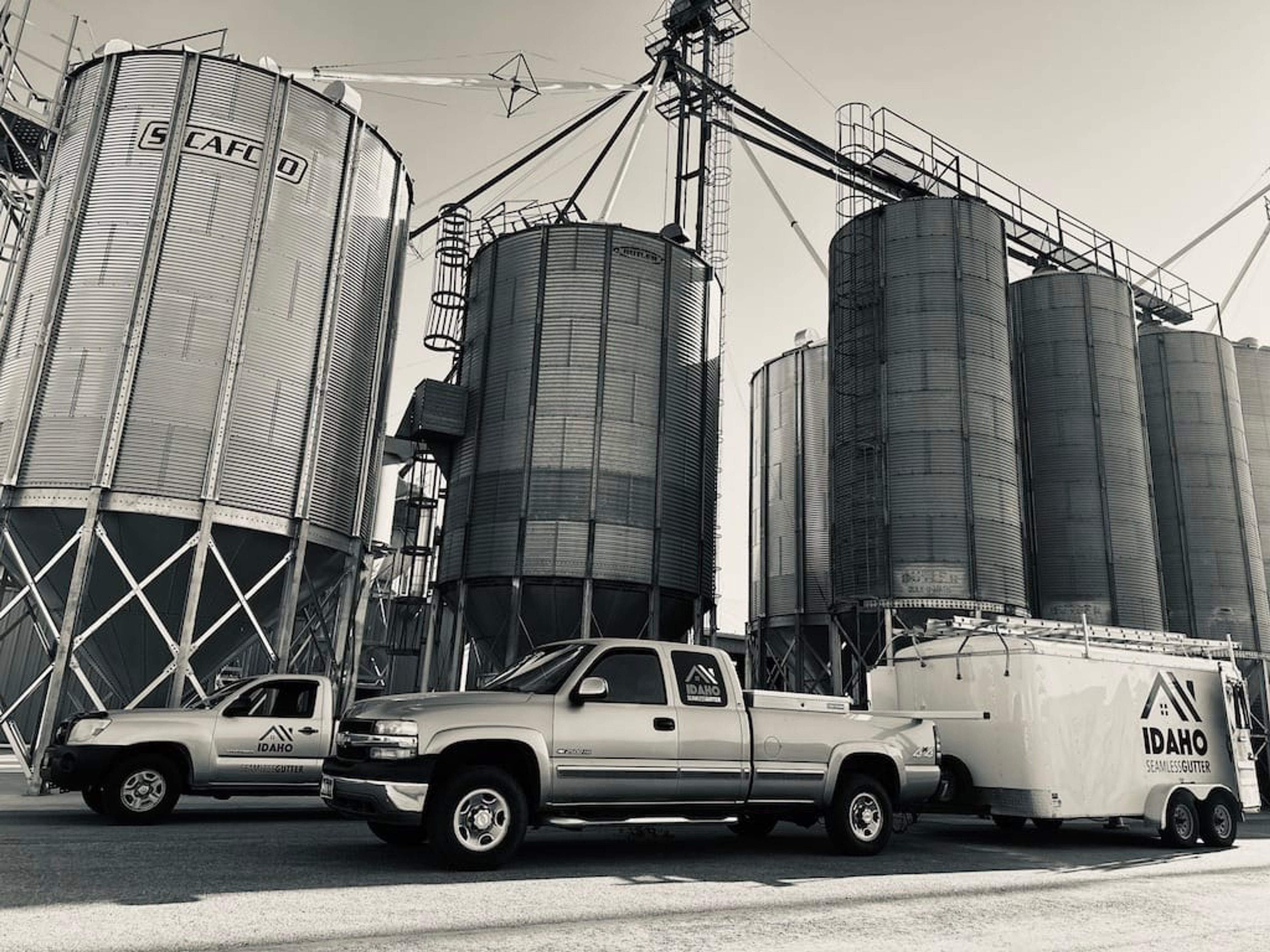 Idaho Seamless Gutter trucks and trailer parked near grain silos in eastern Oregon