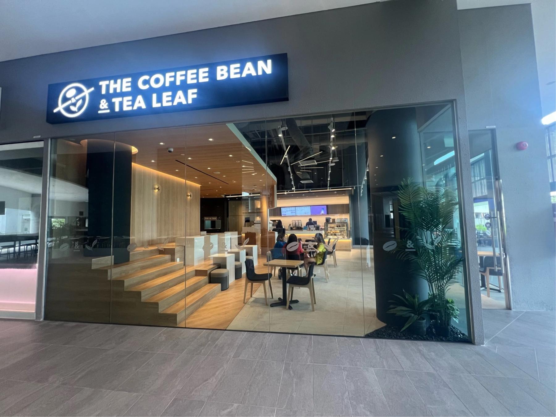 The Coffee Bean & Tea Leaf café storefront inside a modern building, with warm interior lighting and a few patrons seated inside.