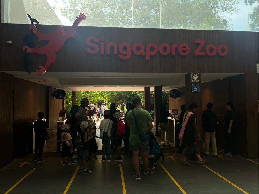 Visitors queuing at the entrance of Singapore Zoo beneath a large red logo sign with a leaping orangutan mascot
