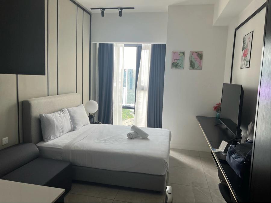 Bright, modern serviced apartment room with a double bed, blue curtains, a flat-screen TV, and a city view through the window
