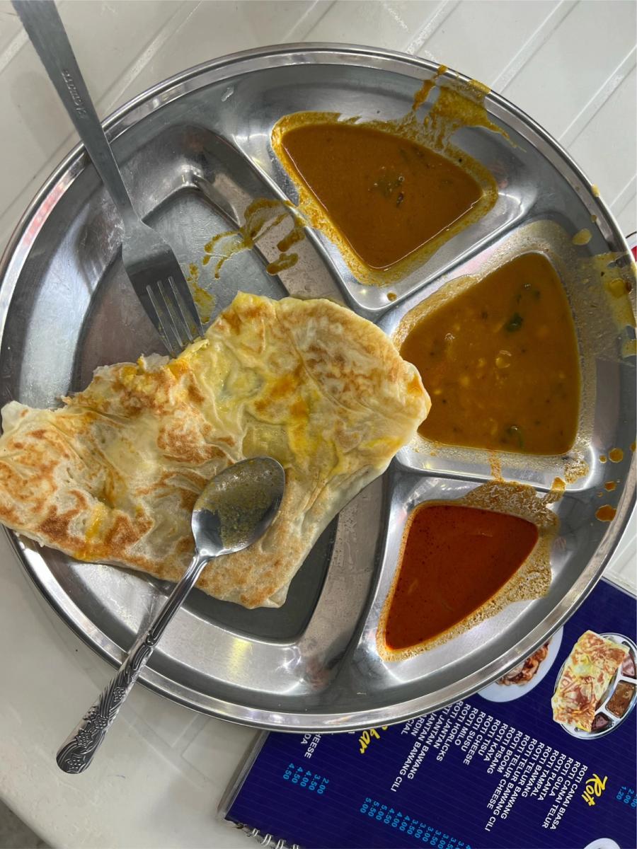 Roti canai telur on a stainless steel divided plate with three dipping sauces — curry, dhal, and sambal — at a KL kopitiam