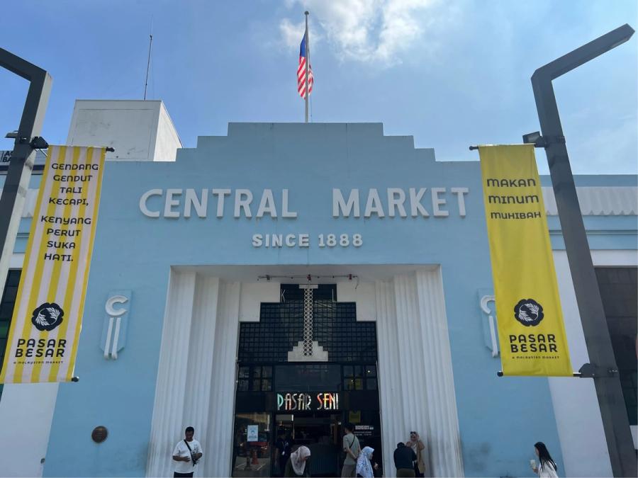 Art Deco facade of Kuala Lumpur's Central Market (Pasar Seni), painted pale blue, with yellow Pasar Besar banners and the Malaysian flag flying above.