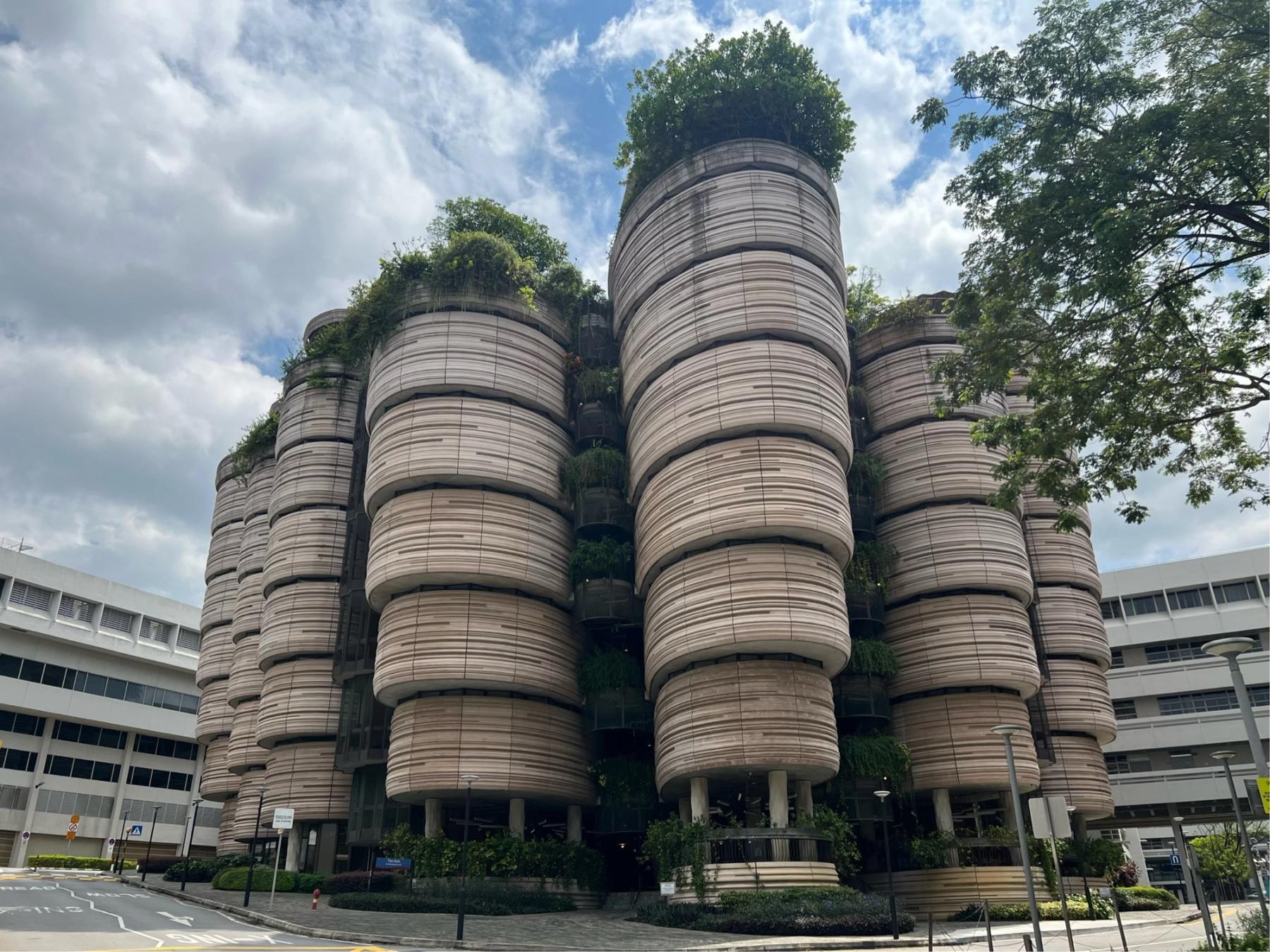 The Hive building at NTU — stacked cylindrical towers with horizontal ribbing and rooftop greenery against a cloudy sky