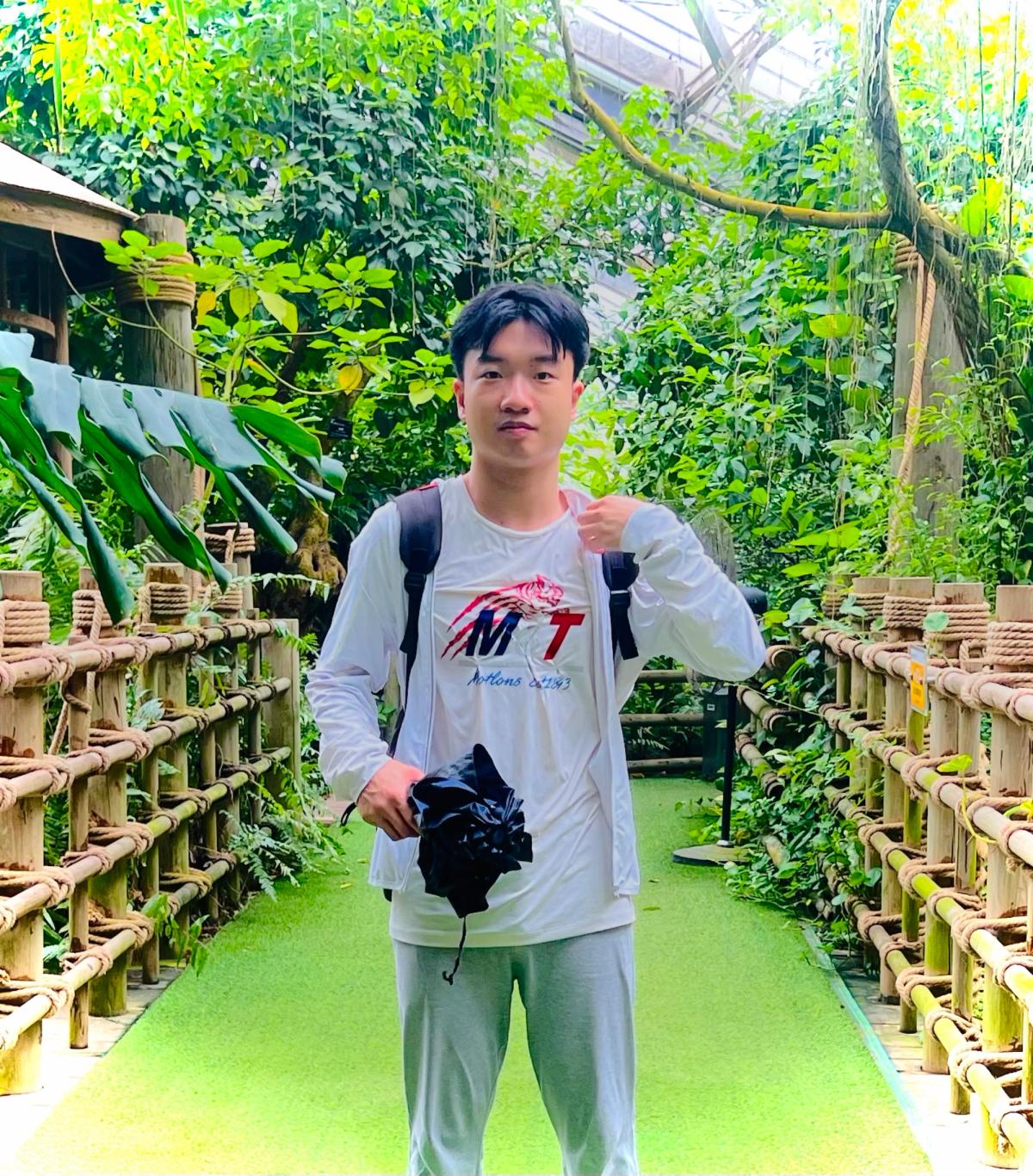 Vito on a wooden boardwalk inside a lush garden conservatory, holding a camera