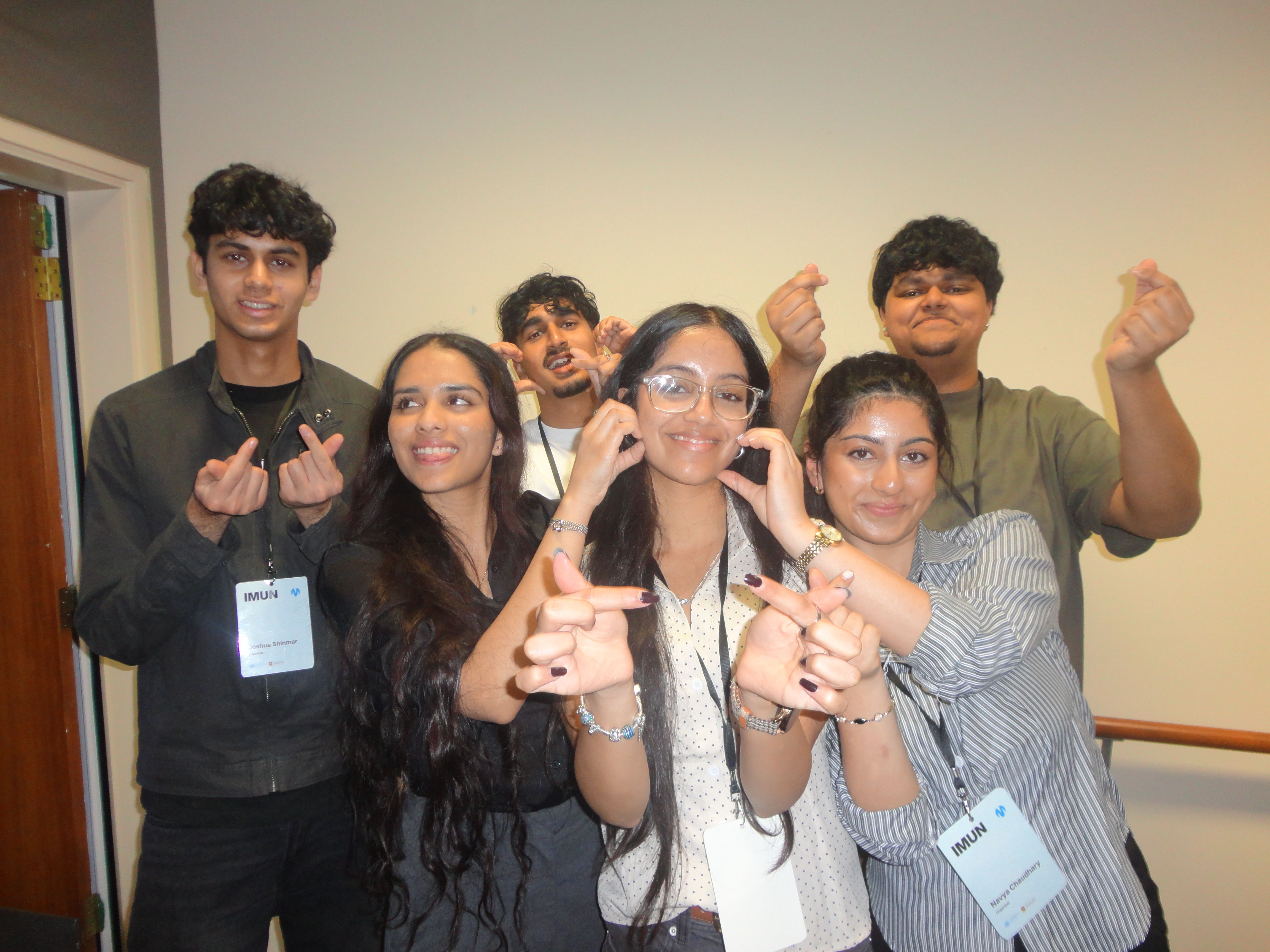 A person with long dark hair, seen from behind, points their thumbs towards themselves outdoors.