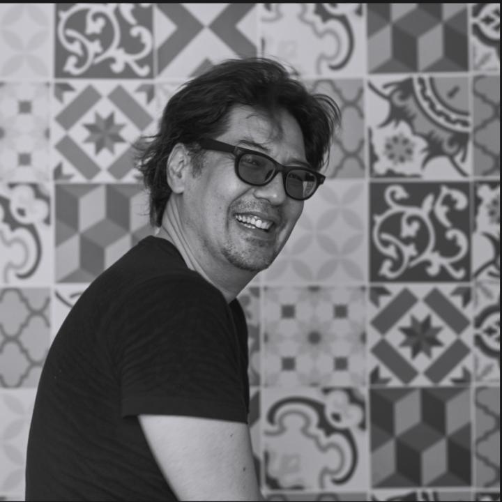 Black and white headshot of Morgan Ommer with a different patterned-tiles wall behind him.