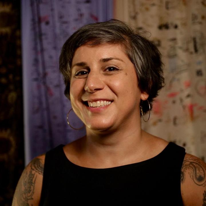 Headshot of Sara Zia Ebrahimi smiling in front of different colored fabrics.