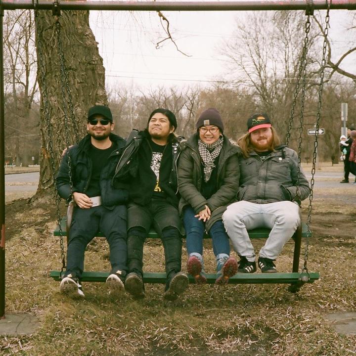 Material Support band sitting on a swinging bench at the park.