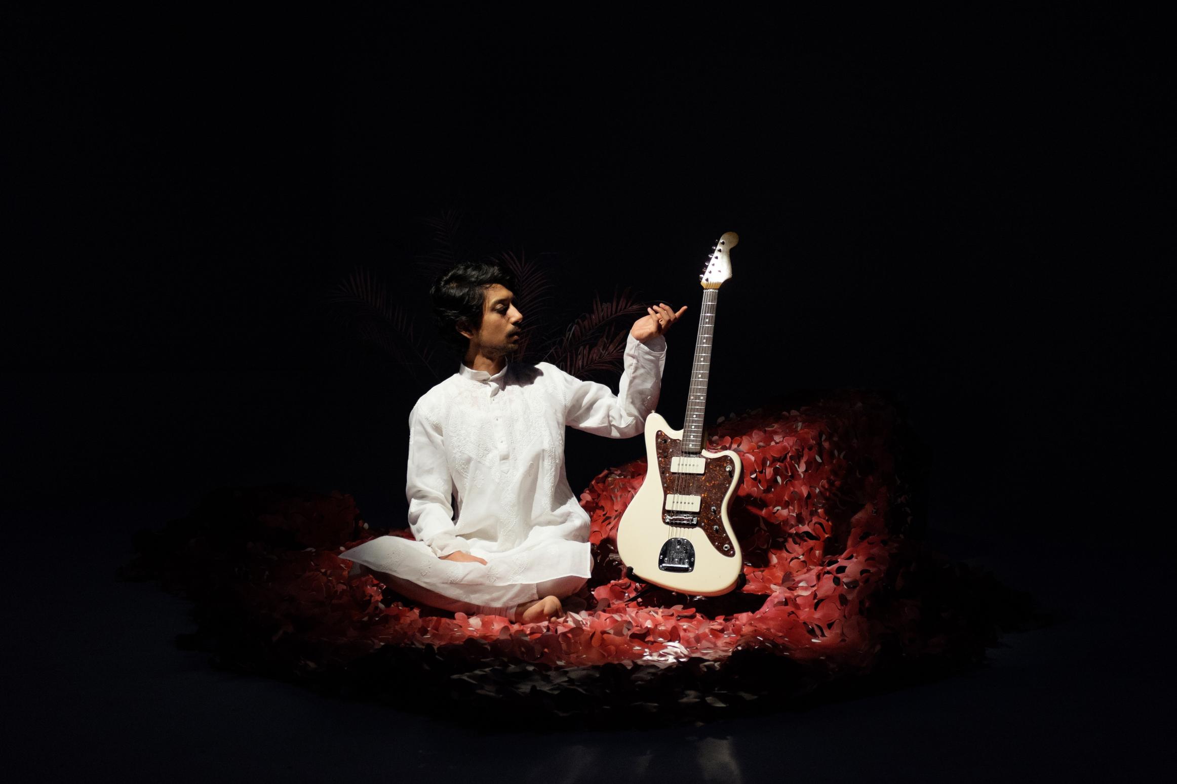 Artist Humeysha sitting on a red carpet next to his guitar.