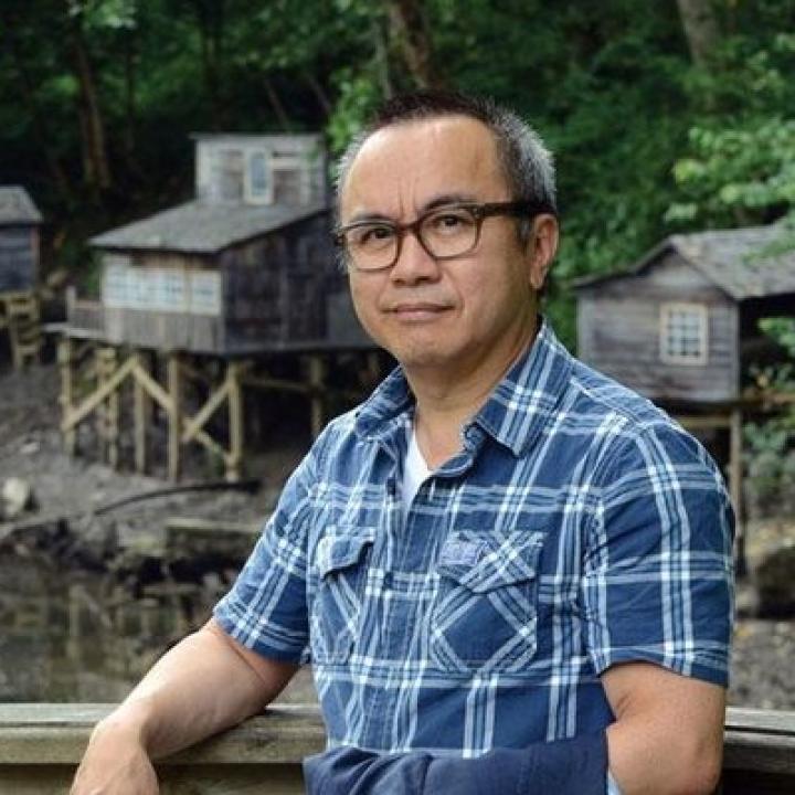 Headshot of Ken Lum with a small, isolated village behind him.