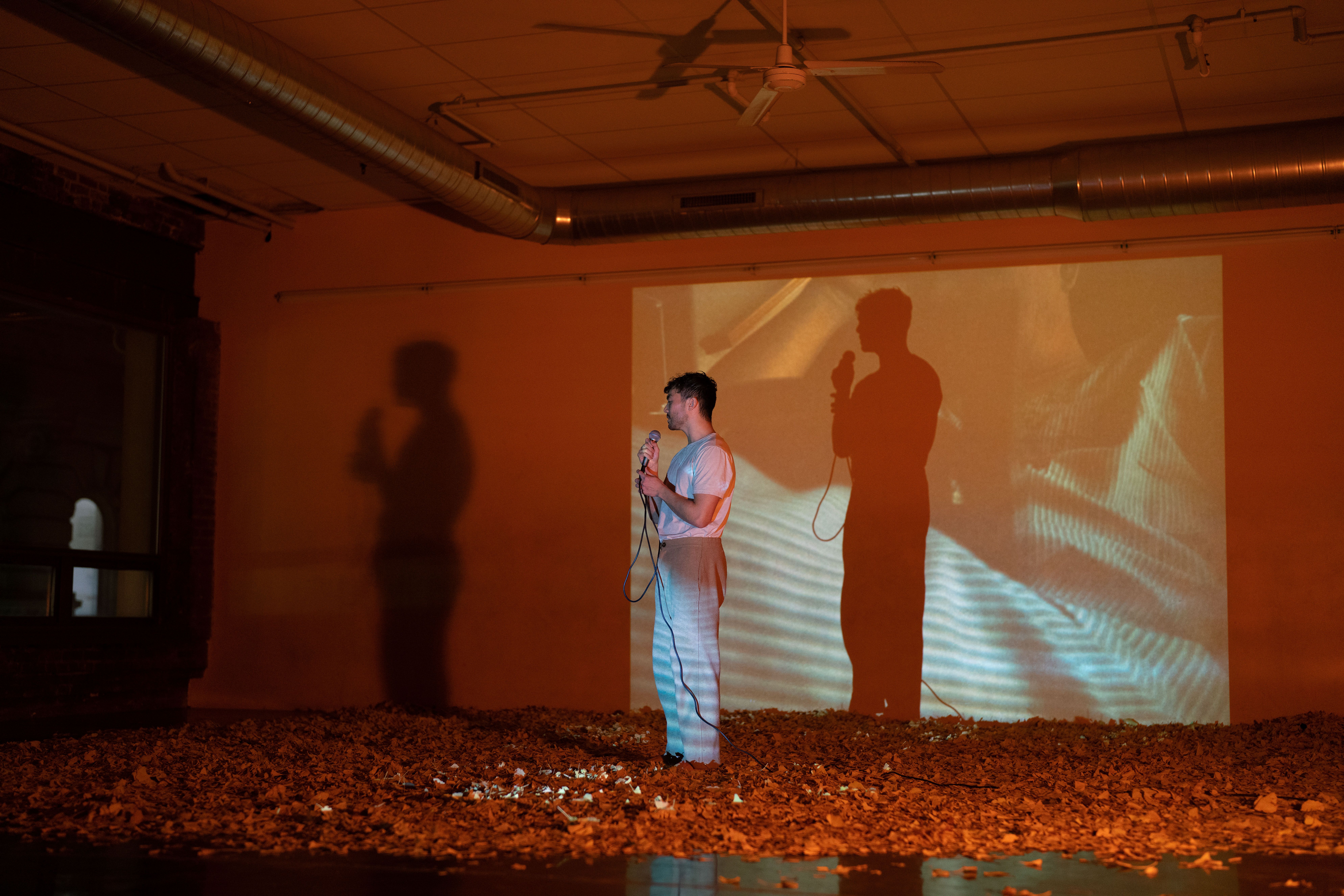 Image of Jason Vu performing in their work "through noise", with abstract projections and gingko leaves covering the floor