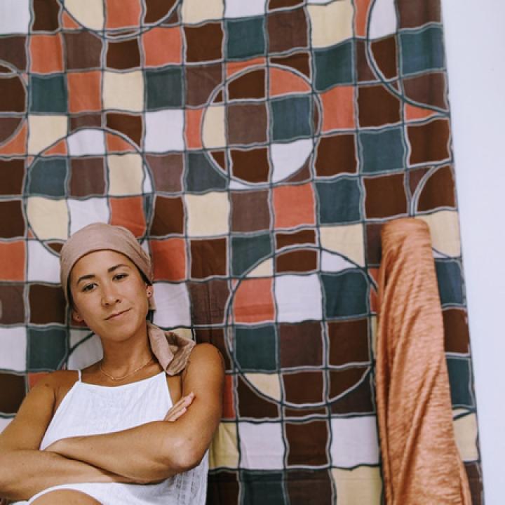 Artist Erica Faria leaning against a colorful, patterned quilt.