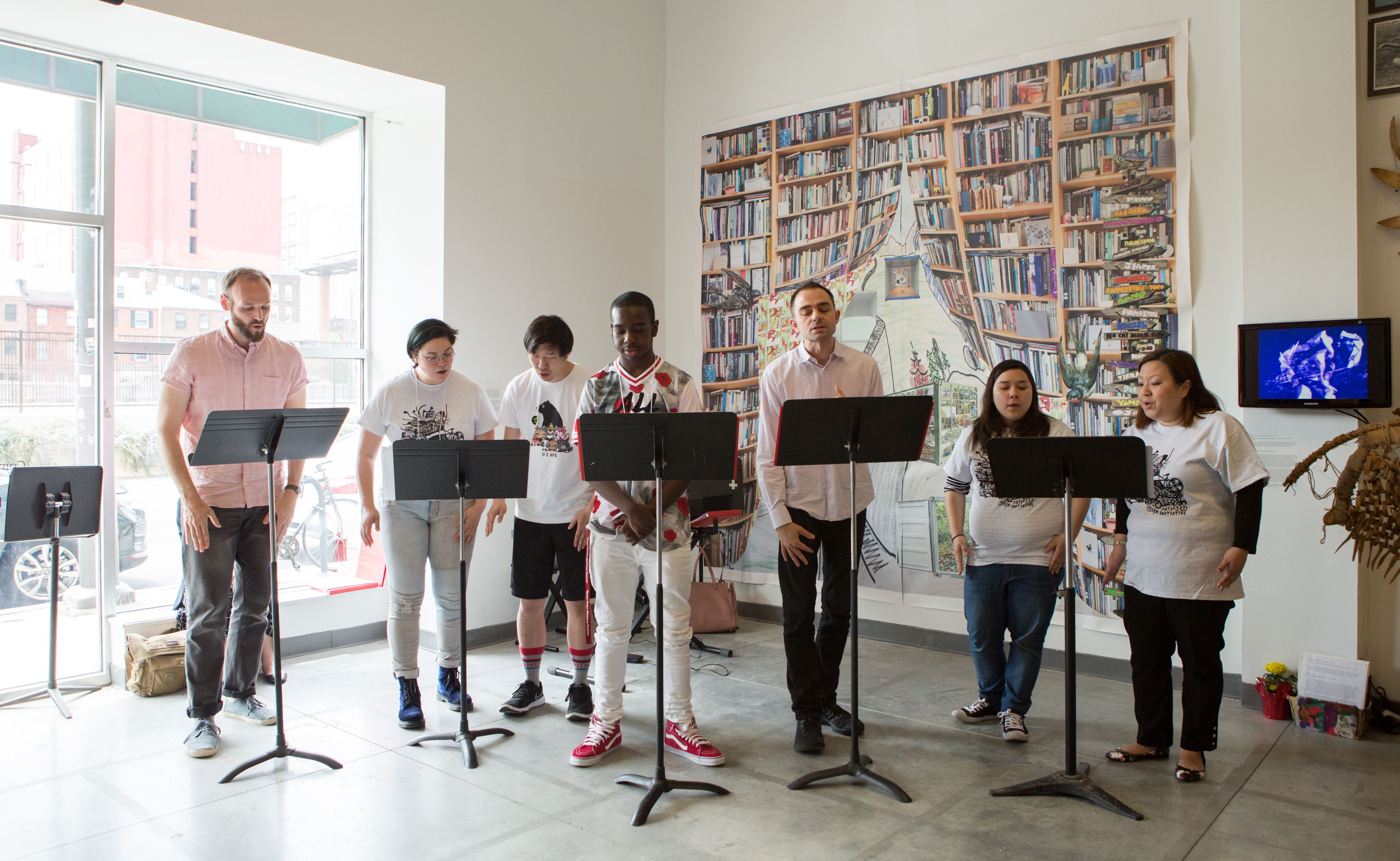 Seven people singing with their own music stands in AAI's gallery