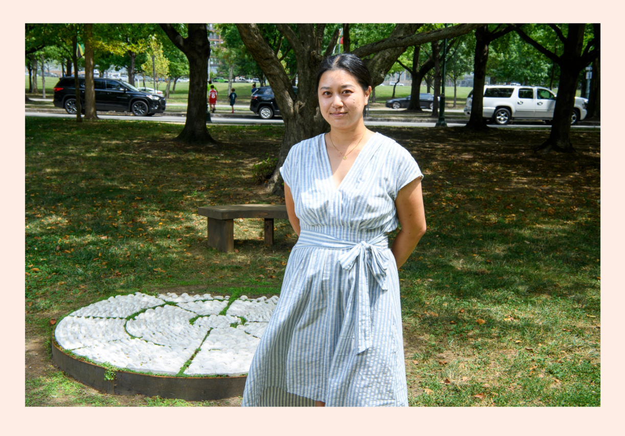 Artist Rachel Hsu standing in front of her public art sculpture made of white pebbles on the ground