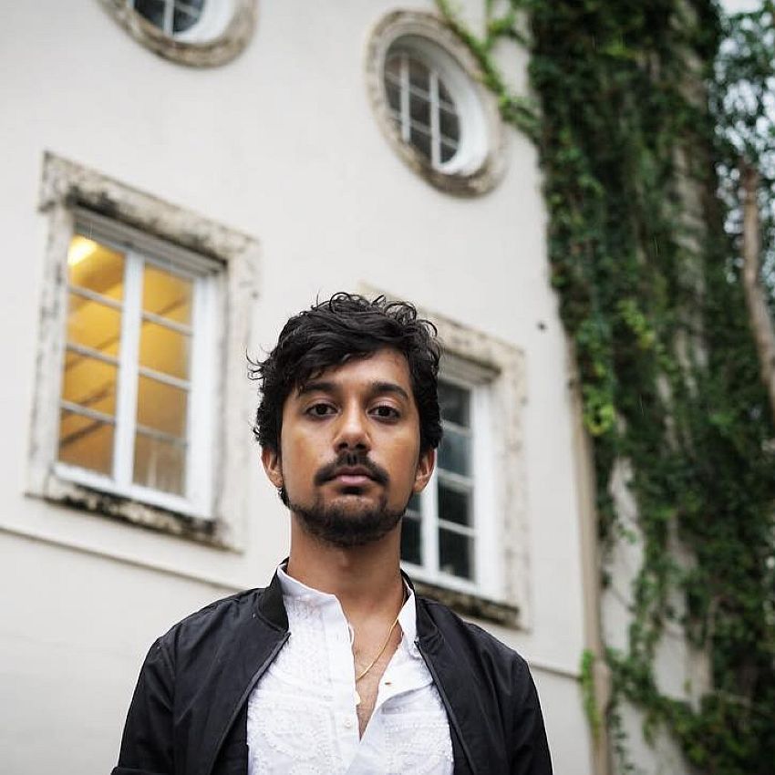 Artist portrait of Zain Alam in front of a white building and a tree