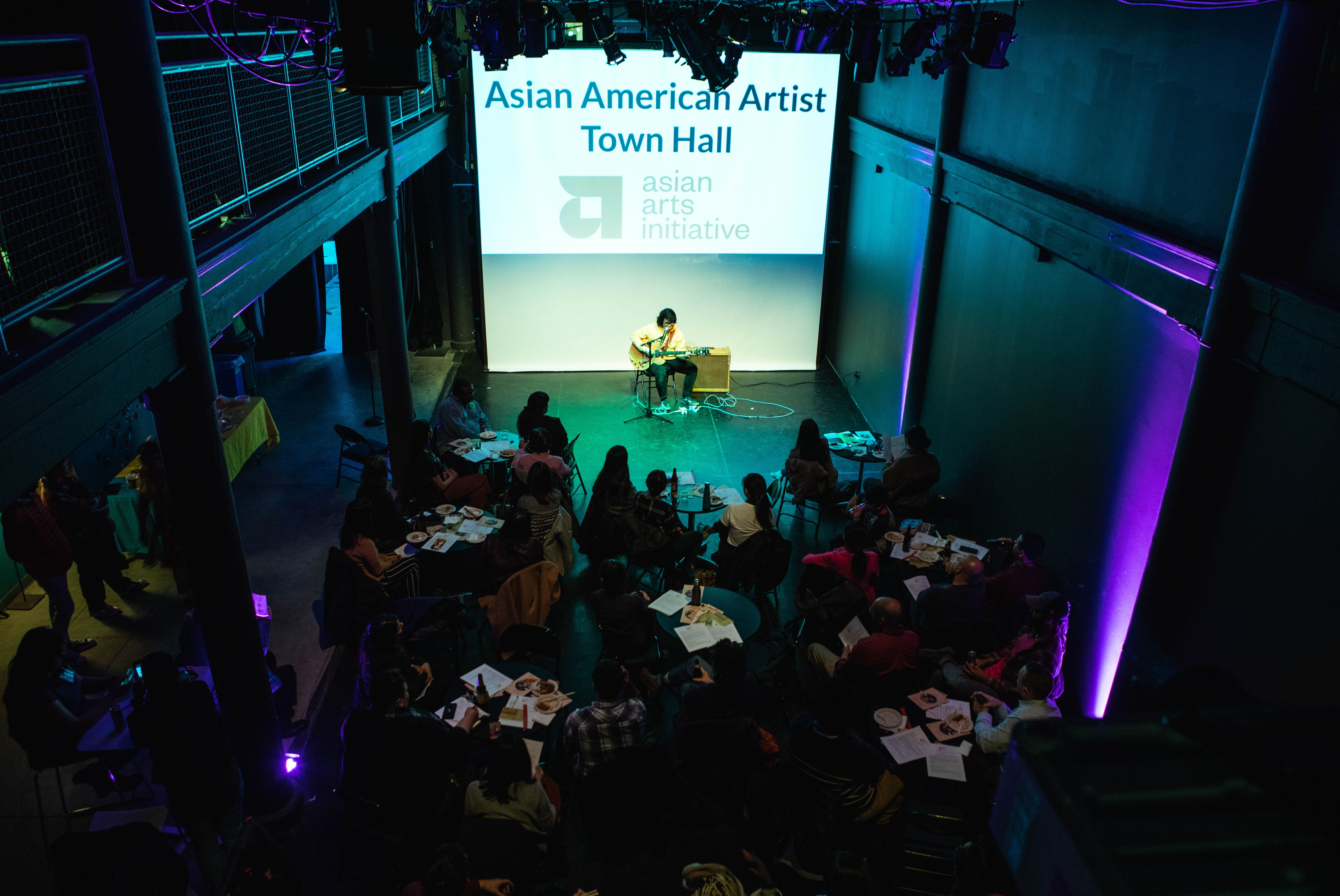 An artist singing and playing their guitar at the Asian American Artist Town Hall.