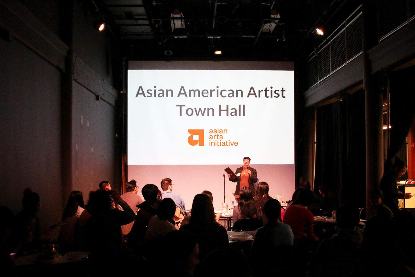 A speaker at the Asian American Artist Town Hall in front of audiences.