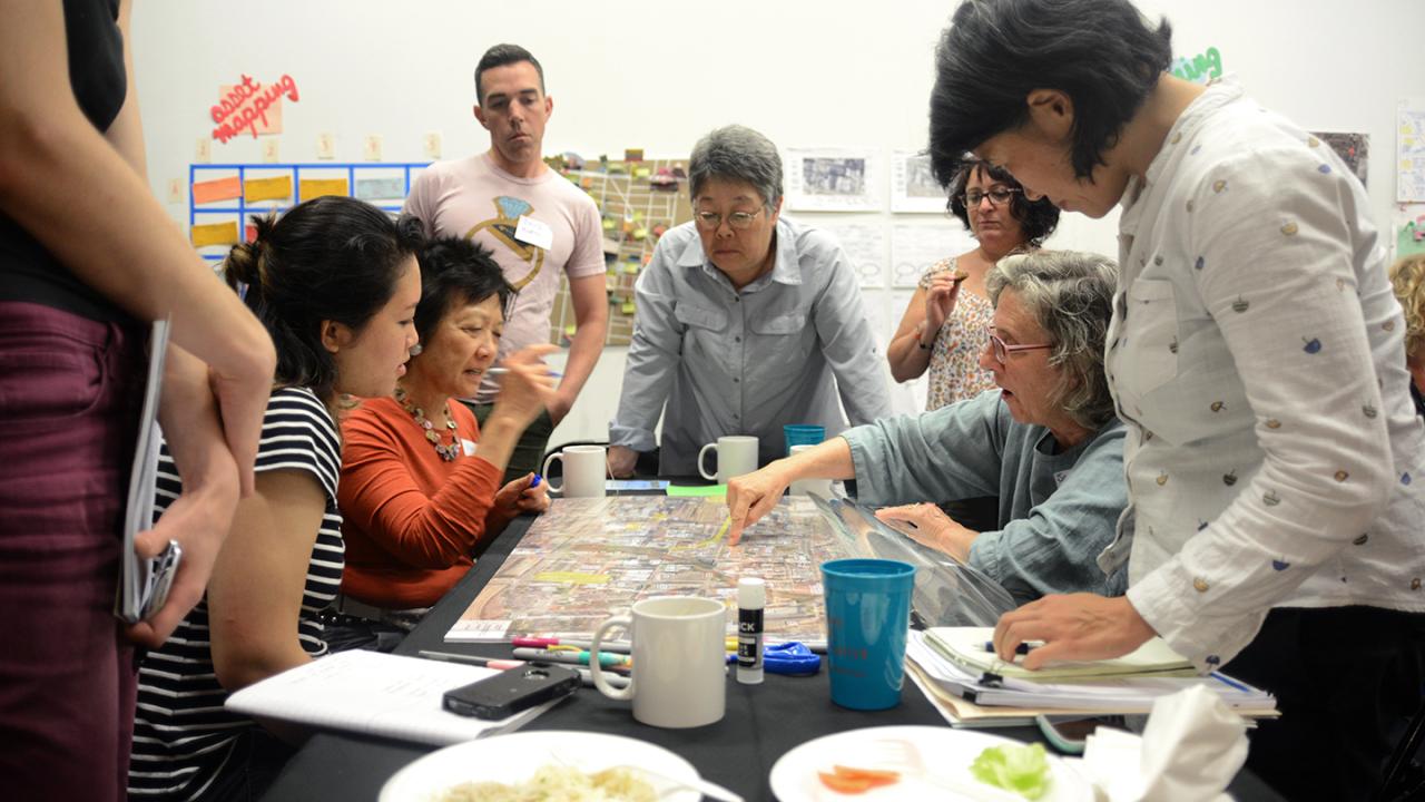 People gathered at a table with a person pointing to a map.