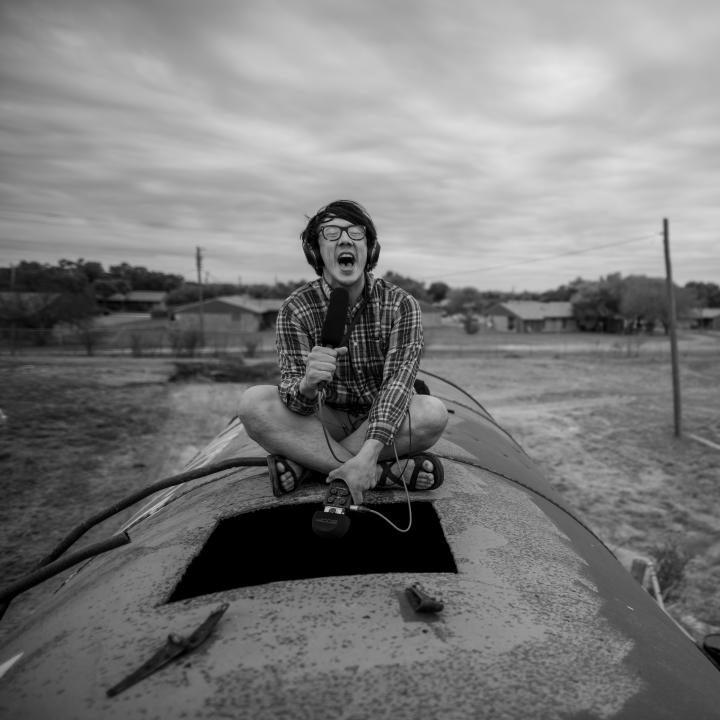 Black and White headshot Artist Julian Saporiti sitting on a large pipe, recording the sounds inside of it.