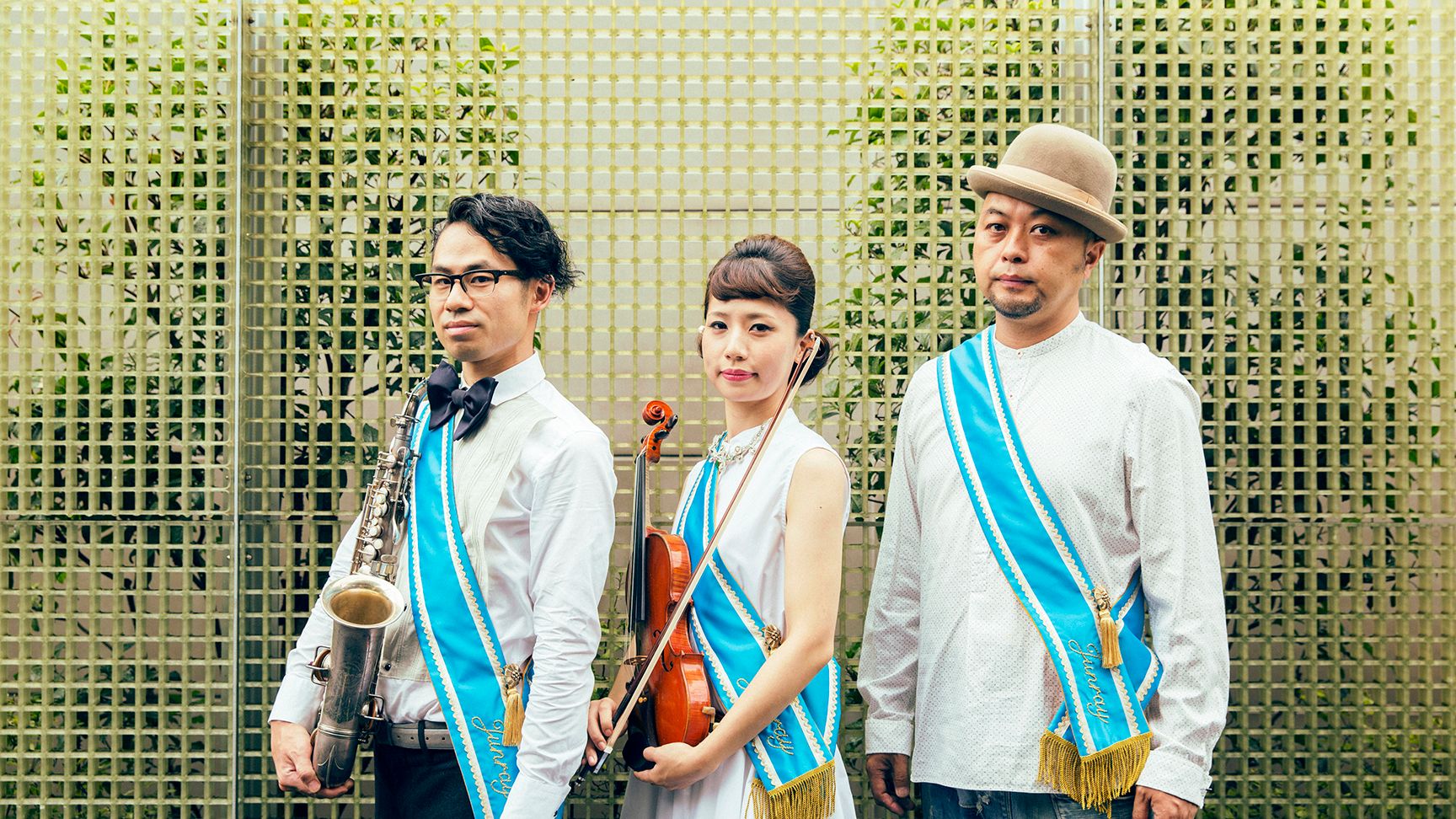 Portrait of the band ASA-CHANG and Junray, a trio of band members wearing blue sash and each holding a saxophone and a violin