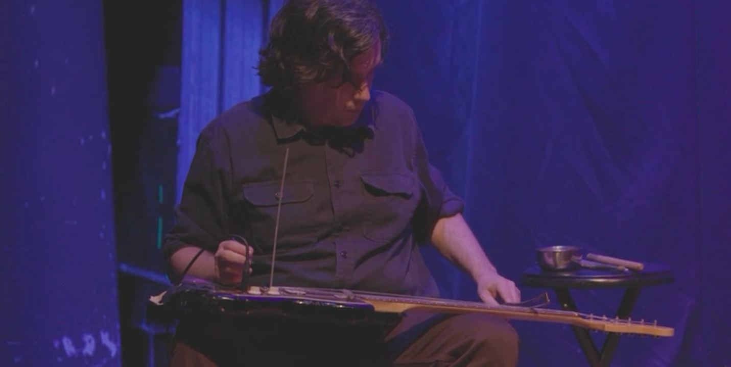 Artist Bill Nace playing an electric guitar with a violin bow