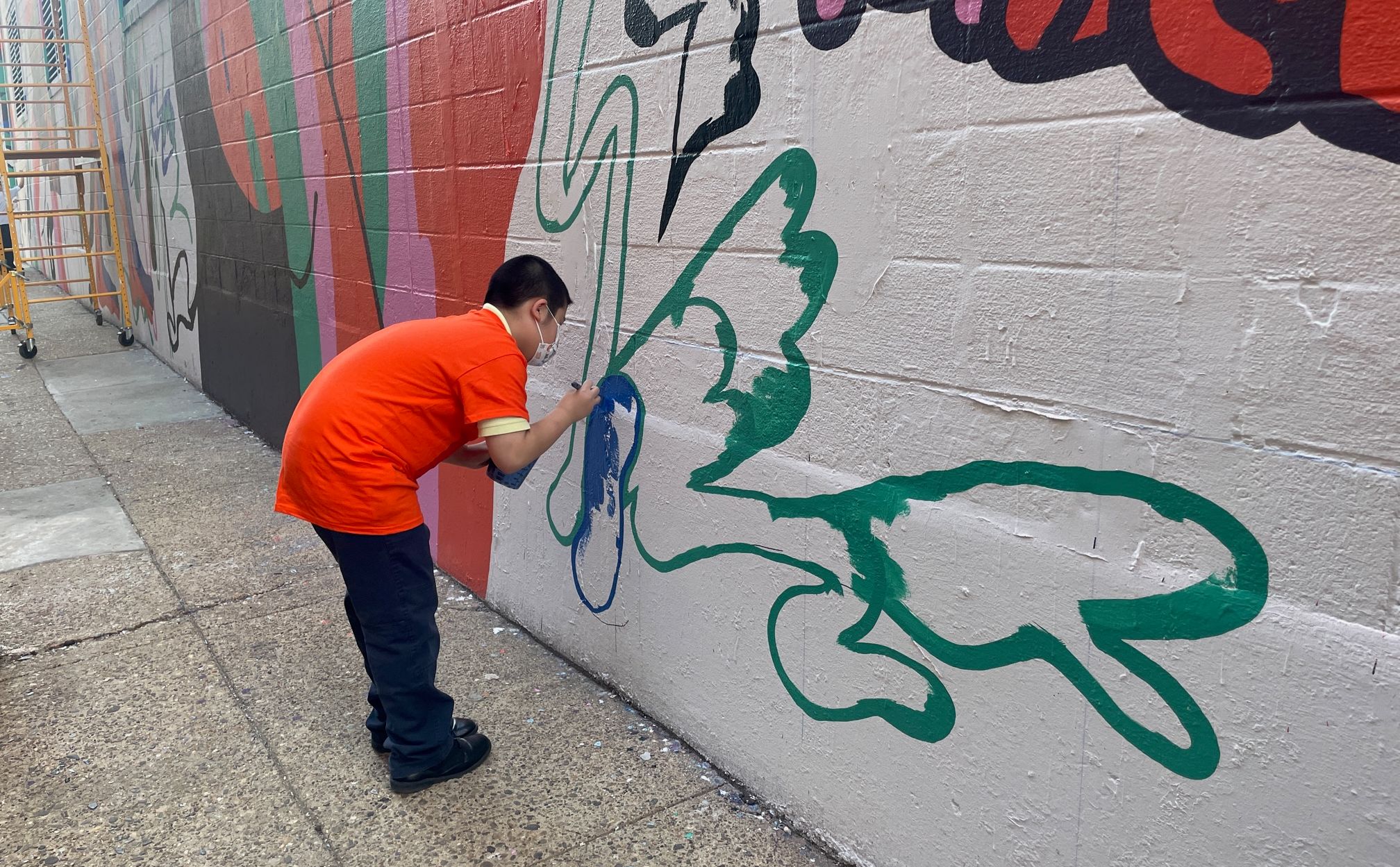 A student painting a mural on the side of a building.