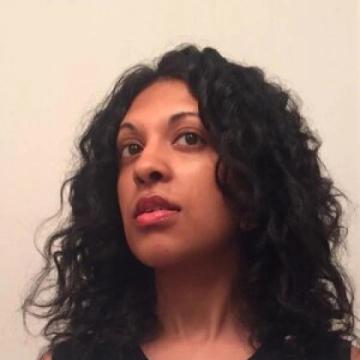 Headshot of Ambika Trasi slightly tilting to the side in front of a white background.