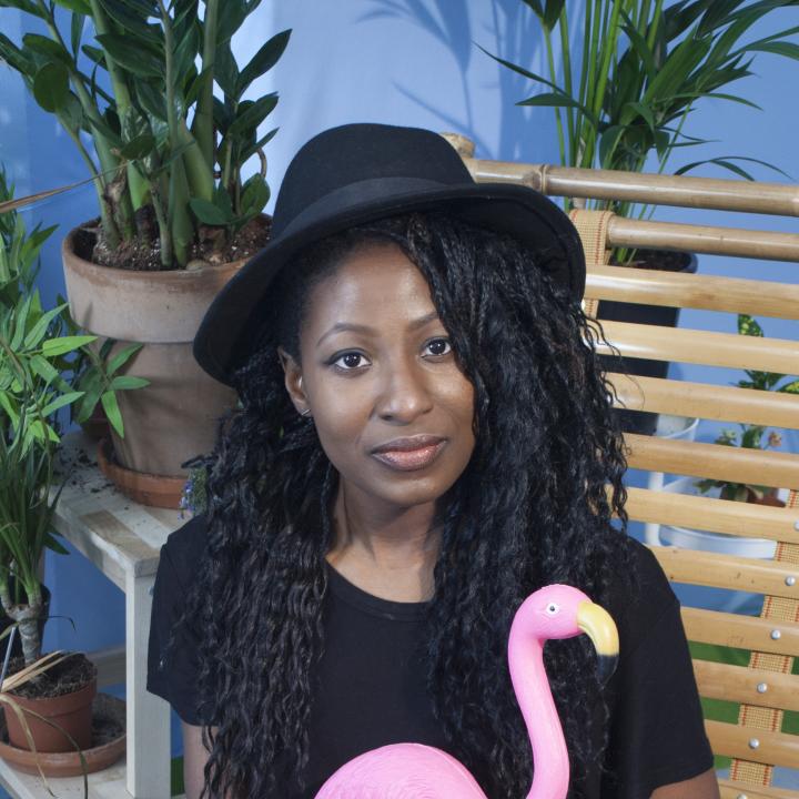 Artist Shannon Lewis sitting down holding a toy flamingo, and plants surrounding her.