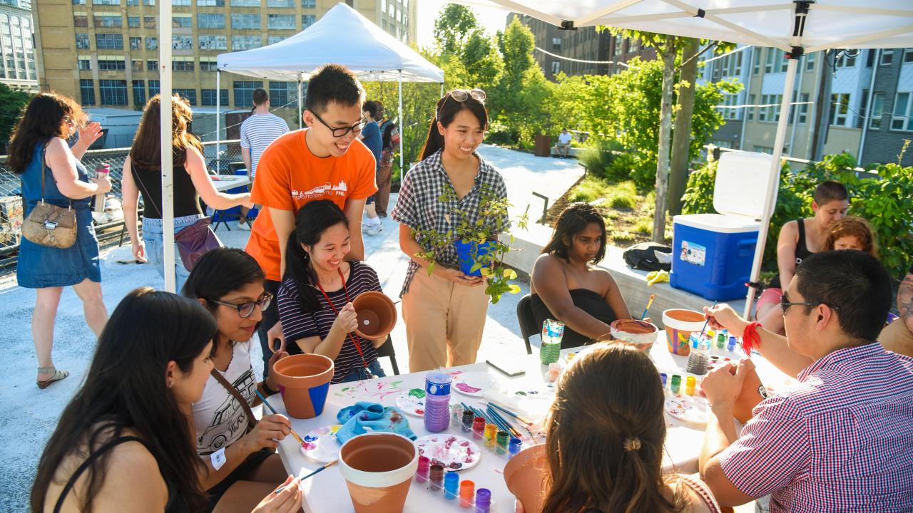 People gathered around a table painting flower pots at railway park.